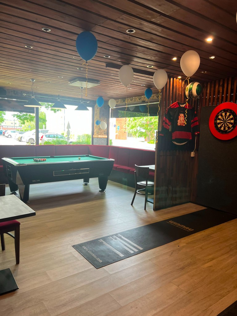 Biljardipöytä, darts ja pelitila ikkunoiden äärellä.